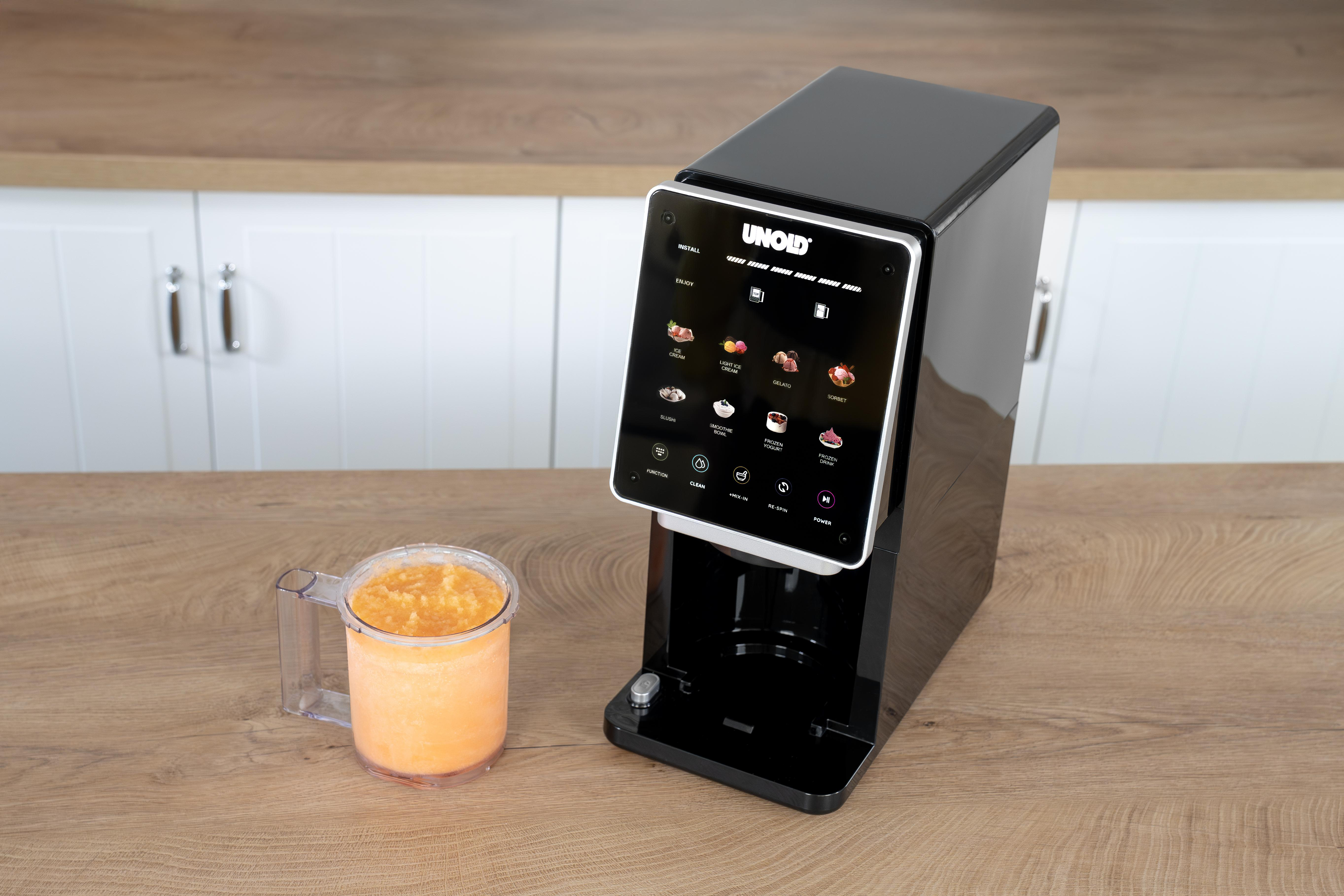 Ein schwarzes UNOLD-Gerät mit Touchscreen daneben ein Glas mit Orangeneis.