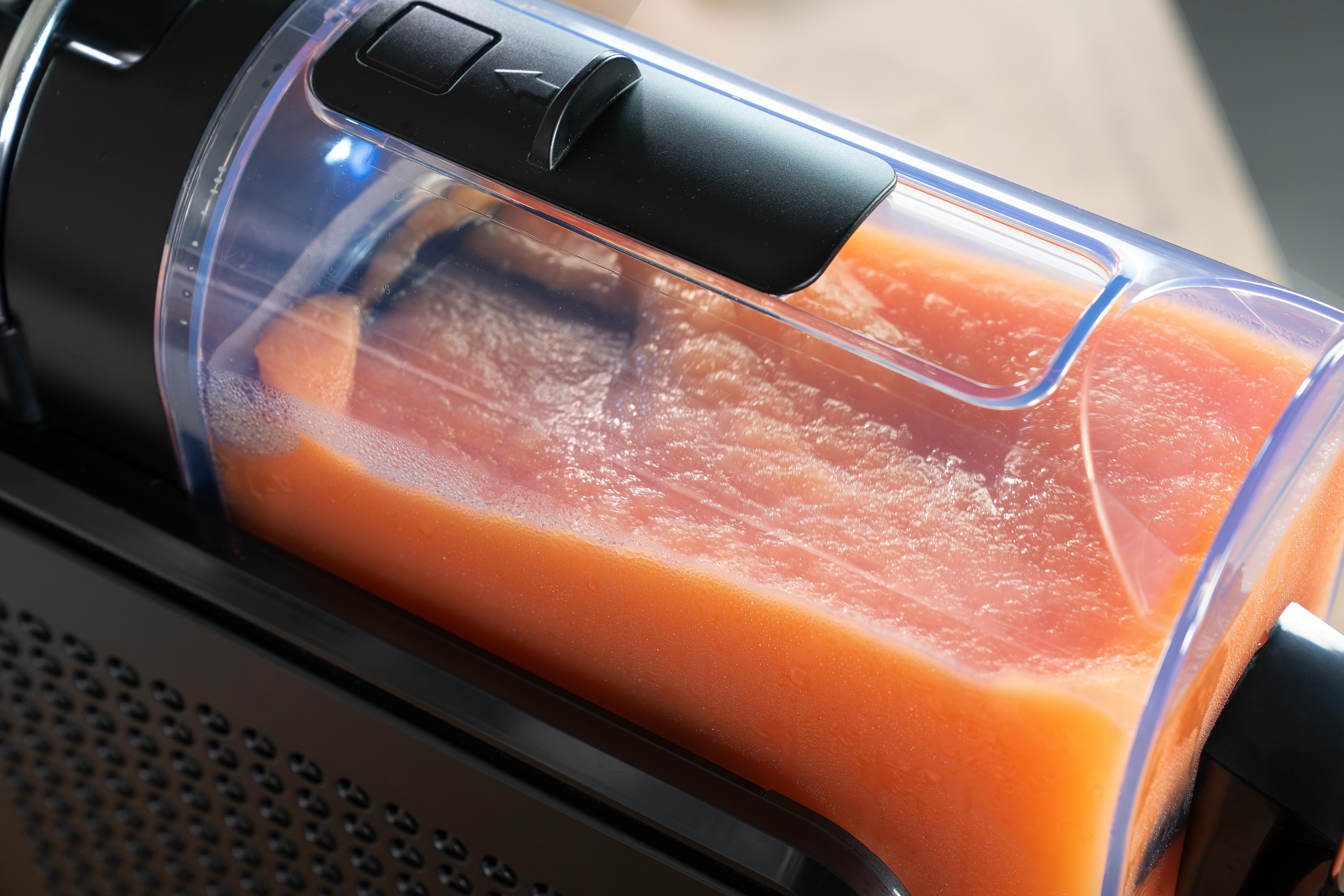 Orangefarbener Saft mit Schaum in einem transparenten Behälter eines Entsafters.