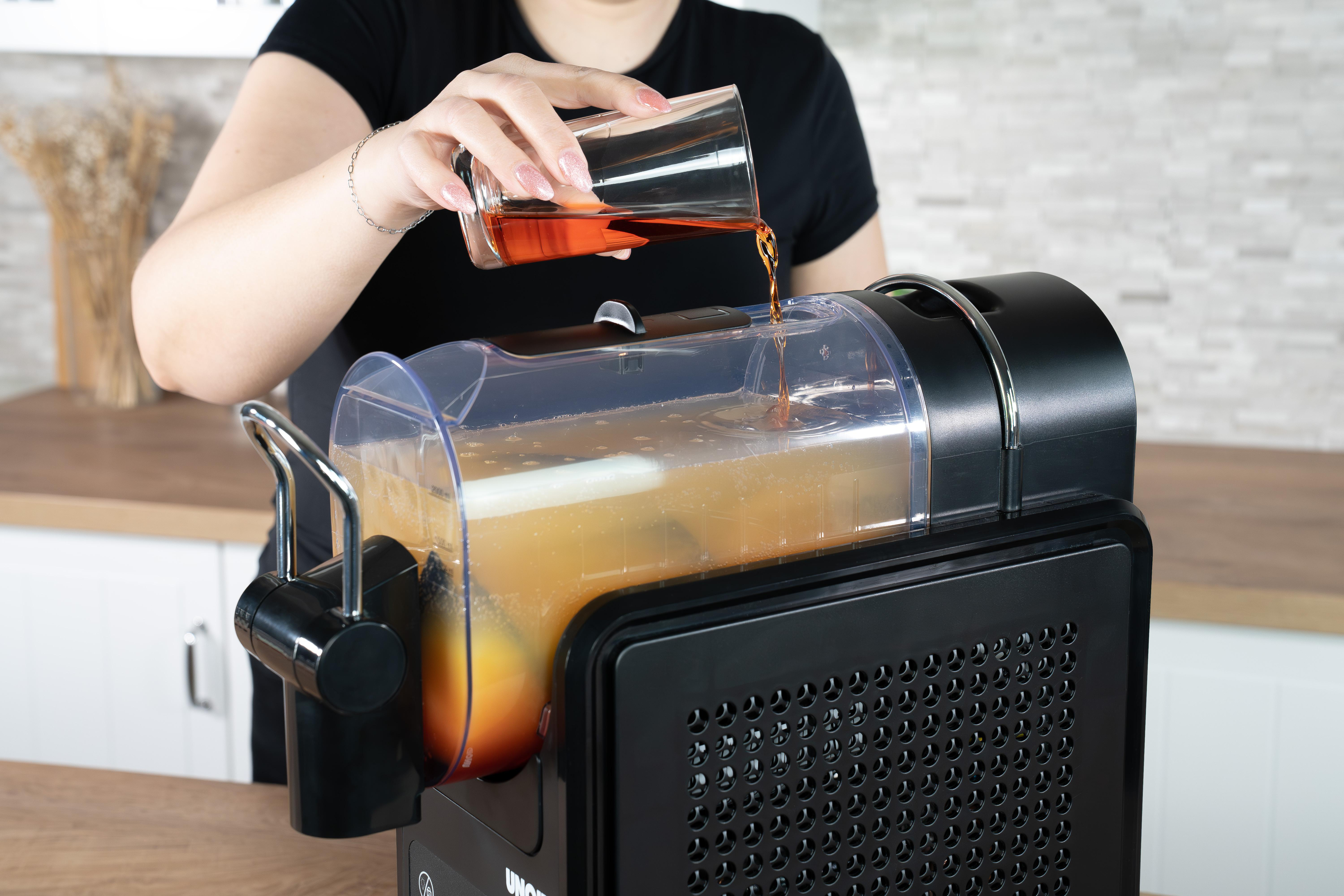 Eine Hand gießt braune Flüssigkeit aus einem Glas in einen Entsafter mit gelbem Saft.