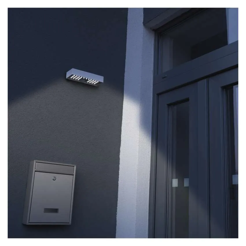 Fehér LED kültéri spotlámpa világít egy sötét falat egy szürke postaláda és egy ajtó mellett.