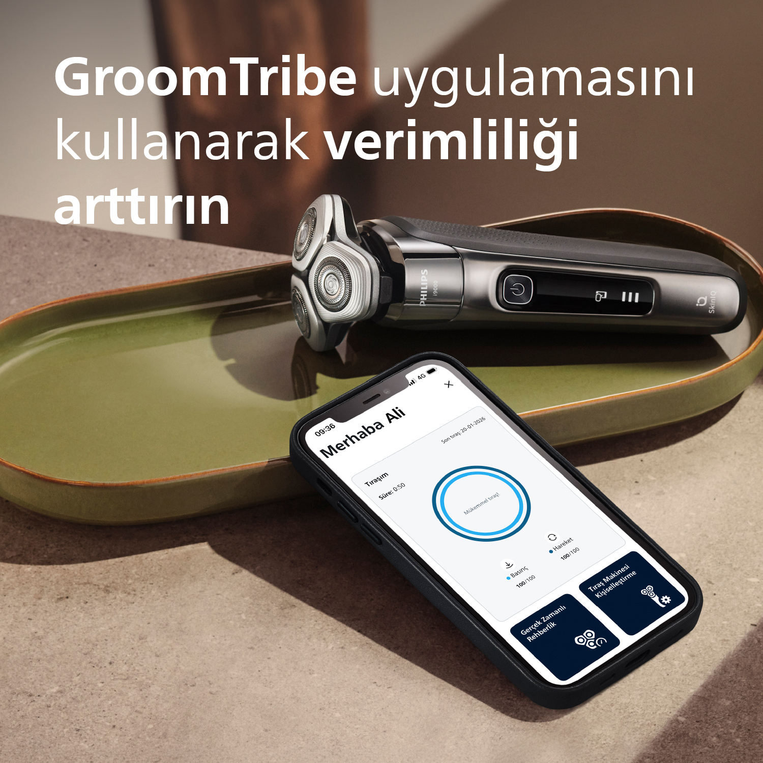 Yeşil bir tabakta GroomTribe uygulamalı Philips tıraş makinesi ve akıllı telefon.