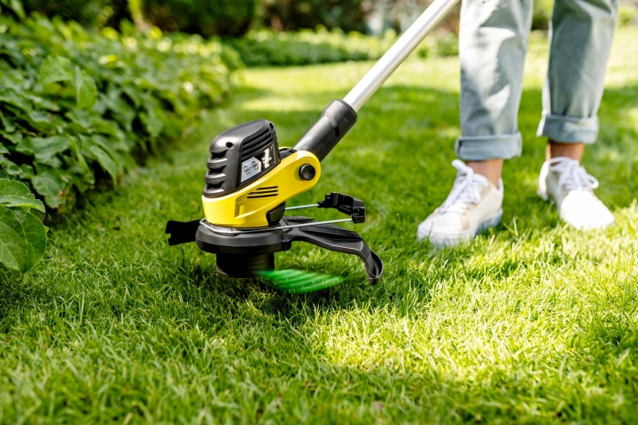 Żółta podkaszarka na zielonym trawniku, osoba w tle.