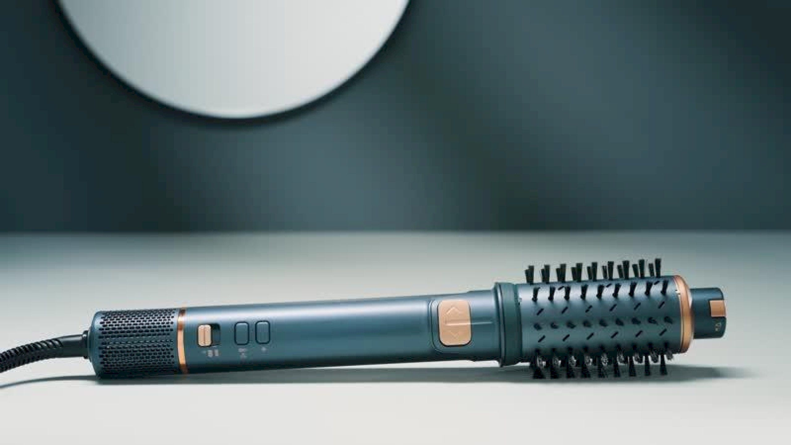 Niebiesko-zielona obrotowa suszarka do włosów z końcówką szczotkową leży na jasnej powierzchni.