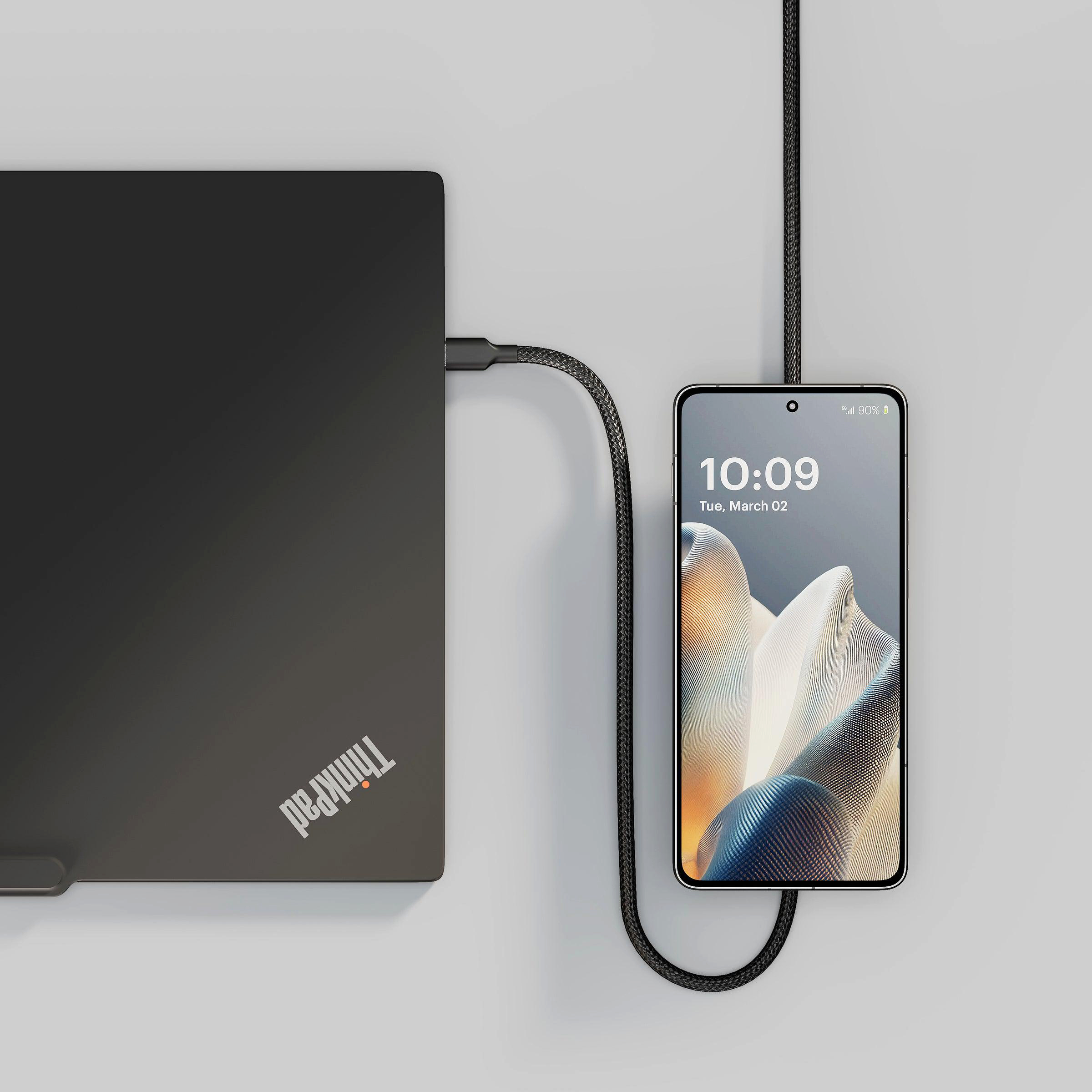 Ein schwarzer Laptop mit ThinkPad-Logo wird mit einem schwarzen Kabel an ein Smartphone angeschlossen.
