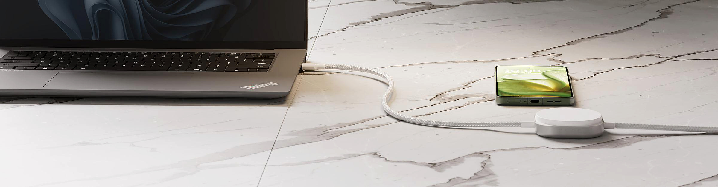 Ein Laptop ist über ein weißes Kabel mit einem Ladeadapter und einem Smartphone verbunden.