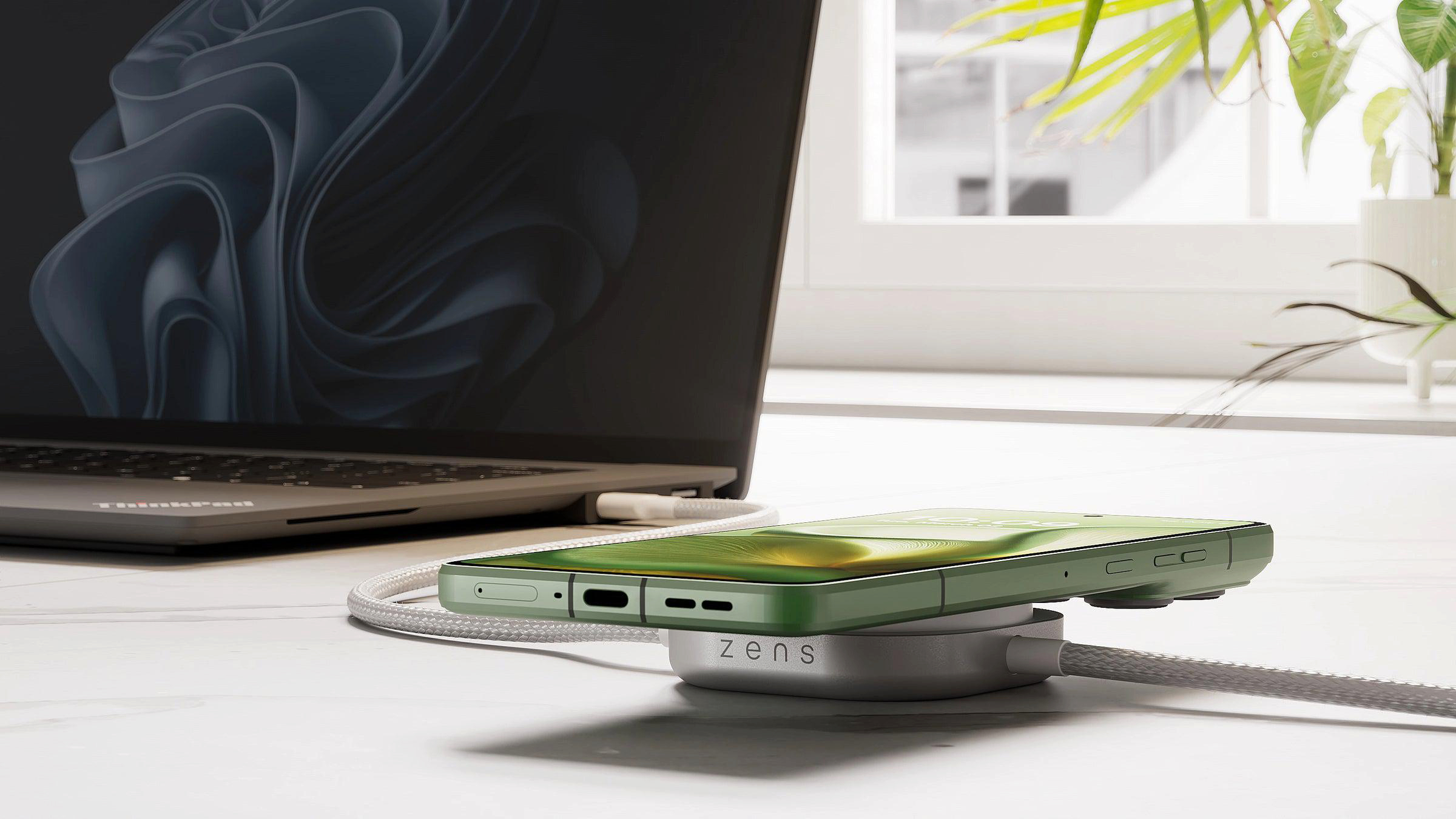 Ein grünes Smartphone lädt auf einer runden weißen Ladestation neben einem Laptop.