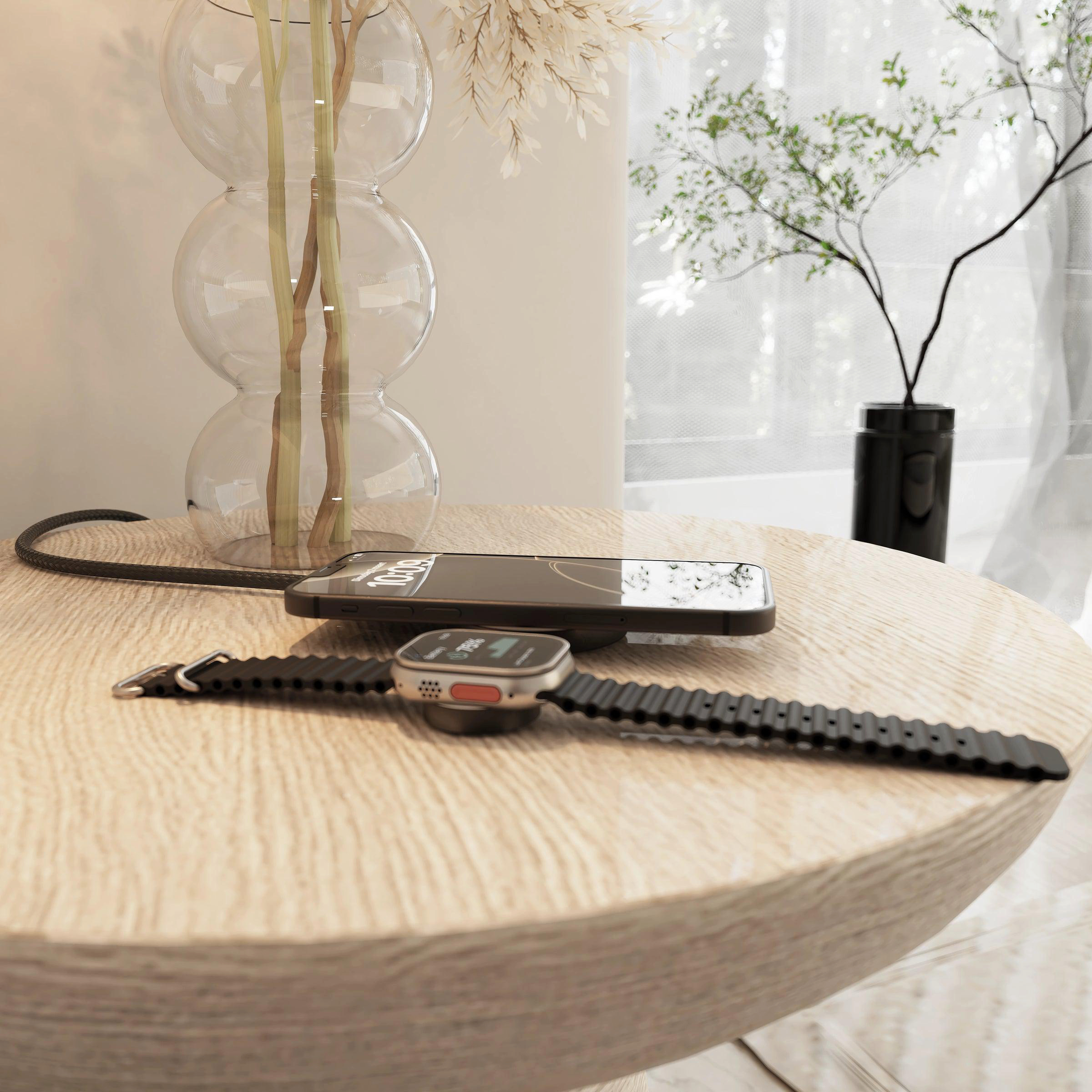 Eine Uhr und ein Handy liegen auf einem Holztisch neben einer Vase mit Trockenblumen.