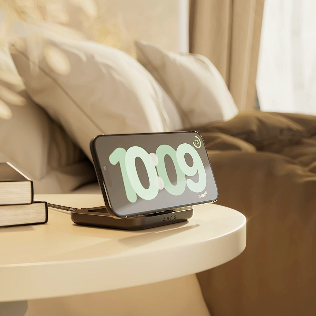 Ein Smartphone zeigt 10:09 auf einem Nachttisch neben Büchern und einem Bett.
