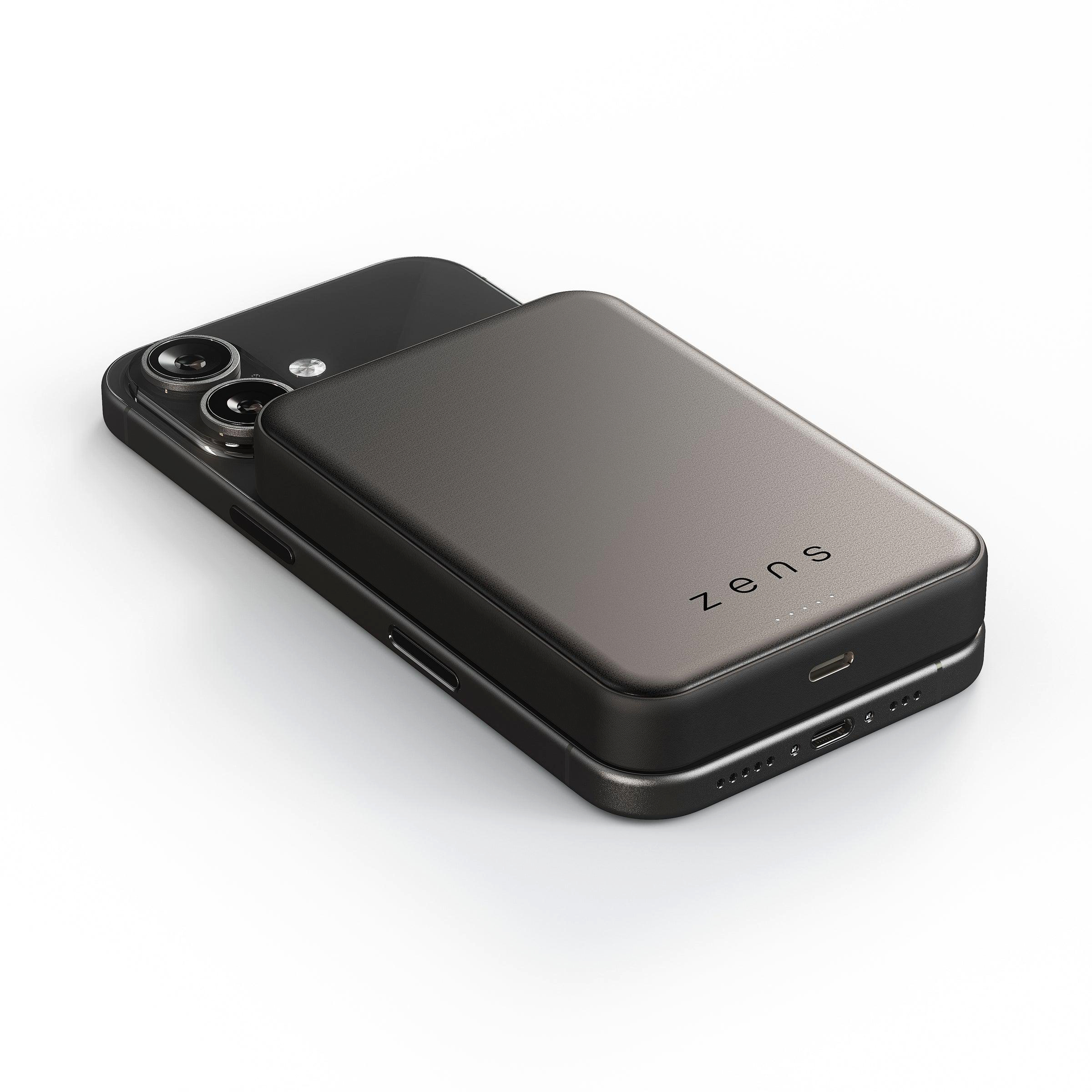 Ein dunkles Smartphone liegt auf einem weißen Hintergrund, mit einem dunklen Ladeakku darauf.