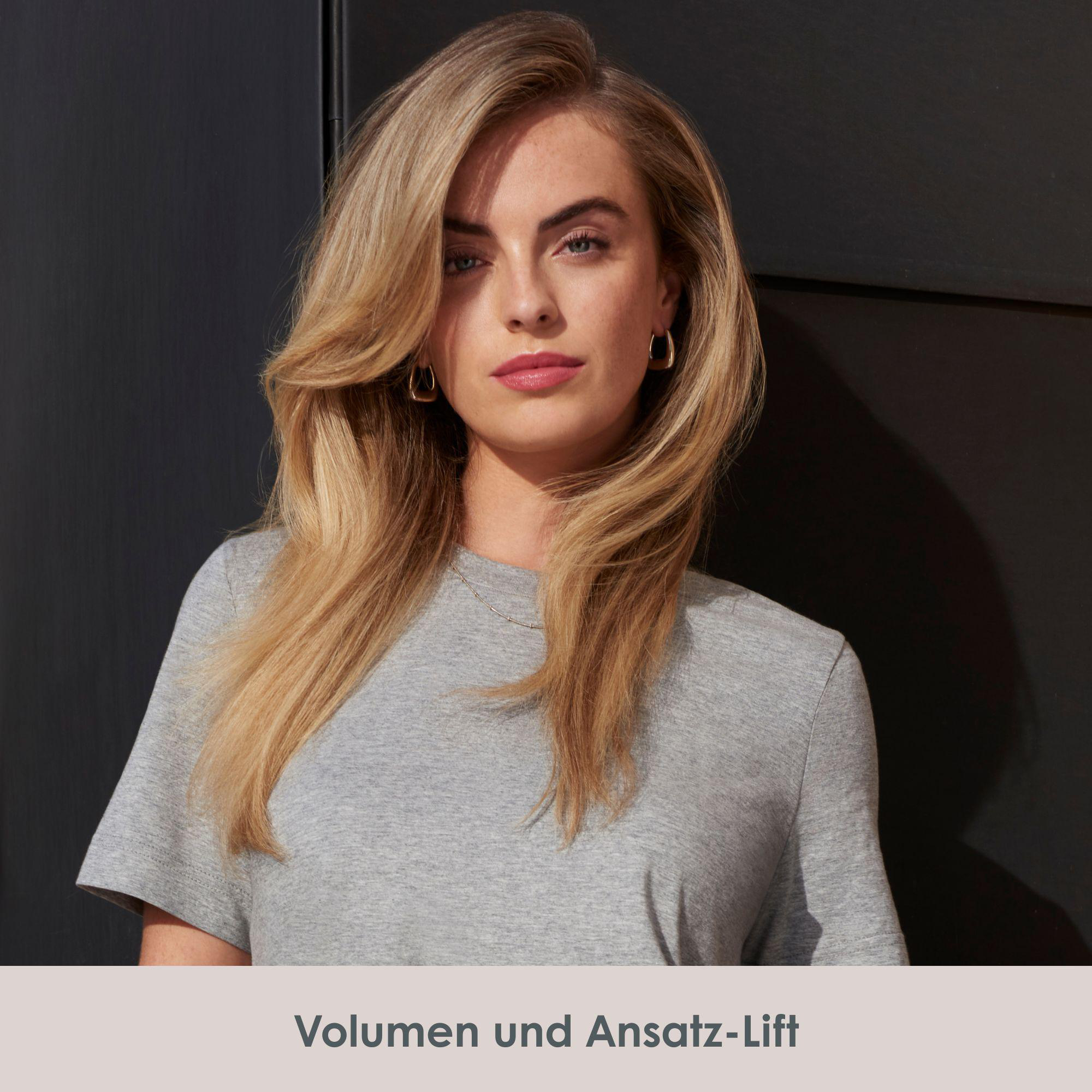 Blonde Frau im grauen T-Shirt blickt in die Kamera, voluminöses Haar.