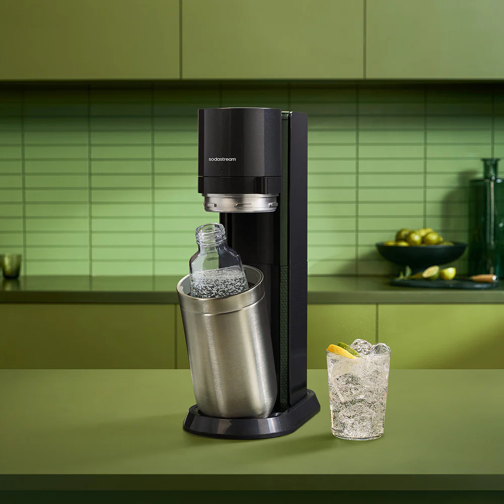 Una máquina SodaStream negra con una botella plateada y un vaso de bebida.