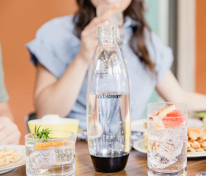 Una botella SodaStream en una mesa con dos bebidas, una con toronja, otra con romero.