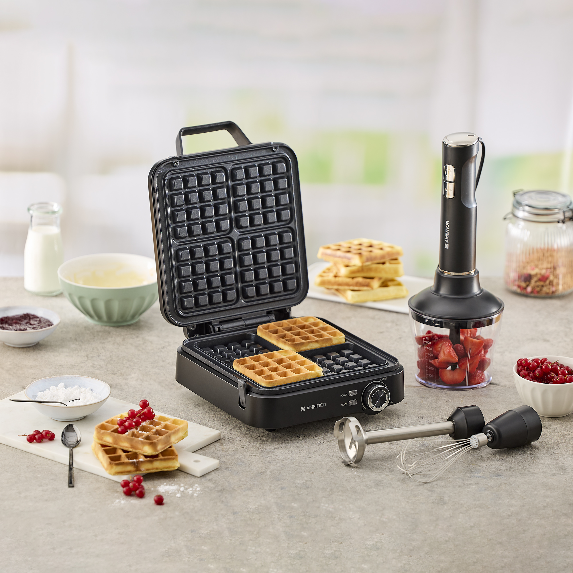 Otwarta gofrownica z dwoma goframi, obok blender ręczny z truskawkami.