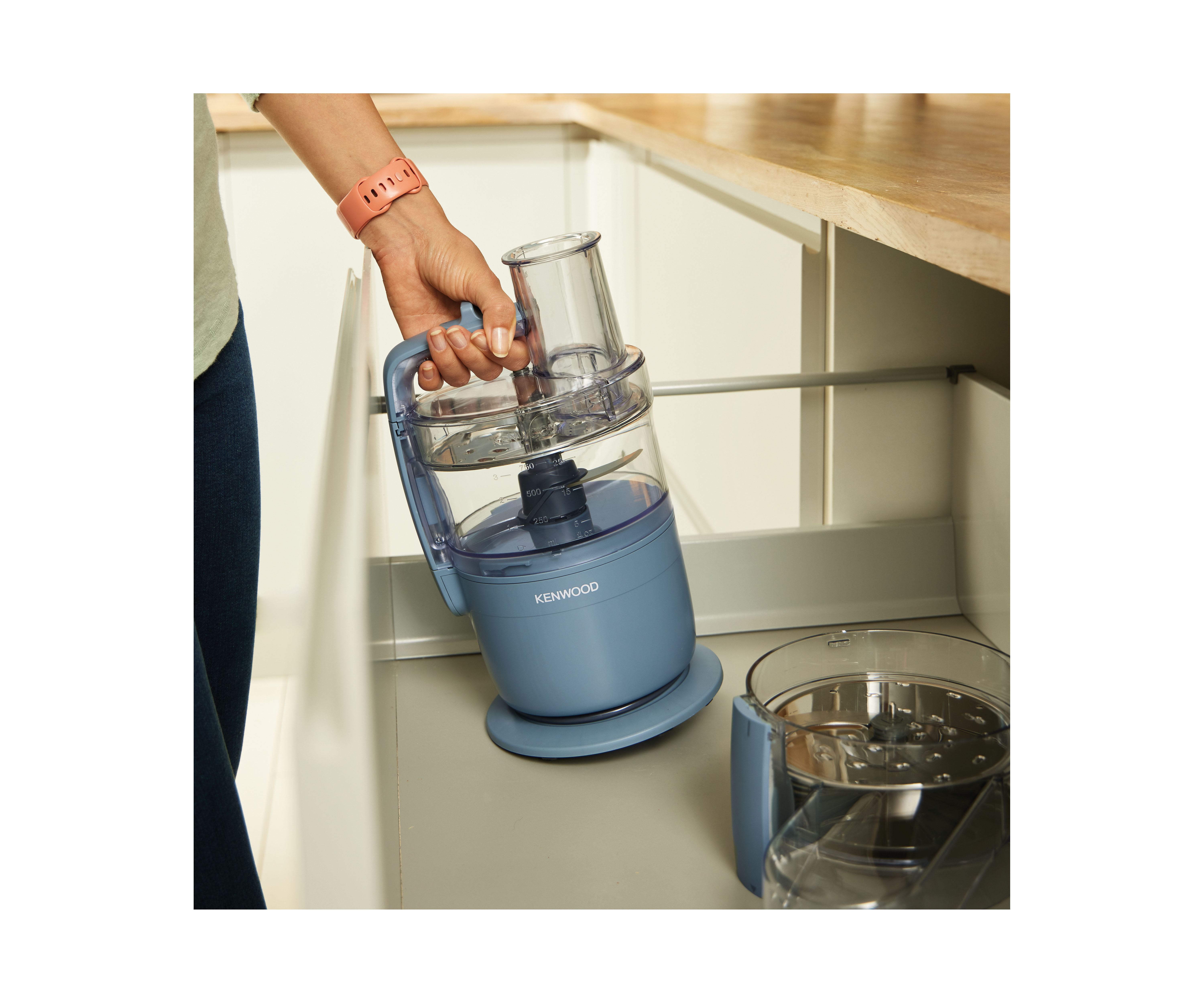 Eine Hand hält eine blaue Kenwood Küchenmaschine mit transparentem Behälter aus der Schublade.