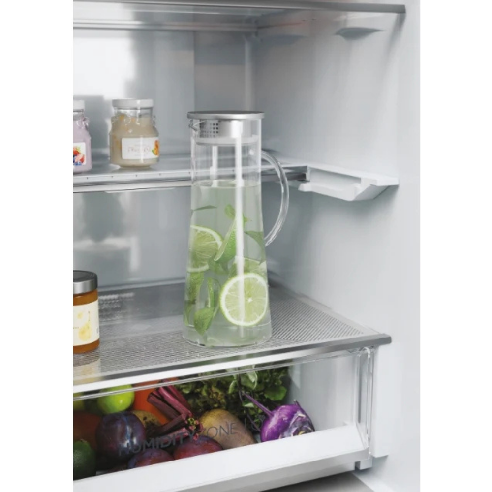 Un estante de refrigerador con una jarra de agua con rodajas de lima y menta.