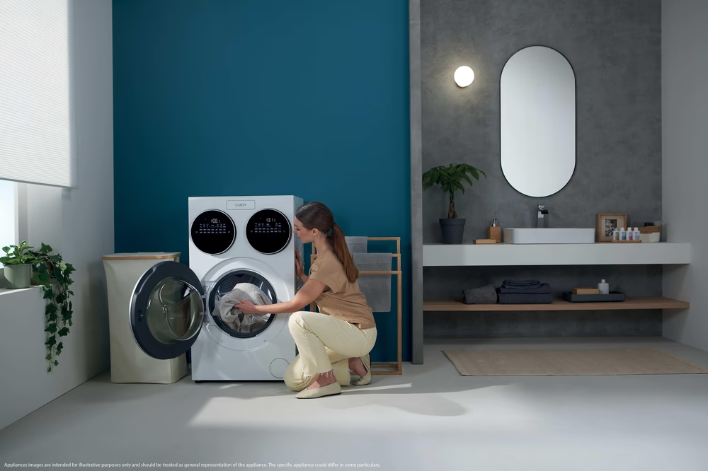 Une femme charge du linge dans une machine à laver blanche dans une salle de bain moderne.