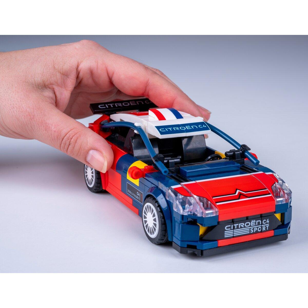 Egy személy egy kék, piros és fehér Lego autót tart CITROËN C4 SPORT felirattal.