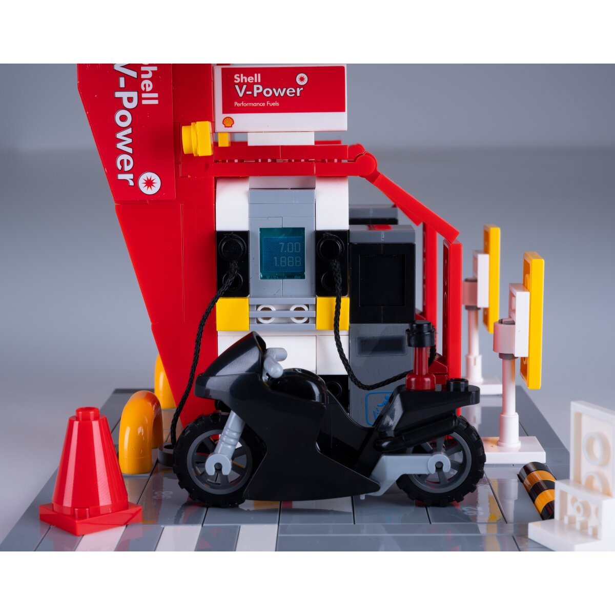Egy fekete Lego motorkerékpár áll egy piros Shell V-Power benzinkútnál digitális kijelzővel.