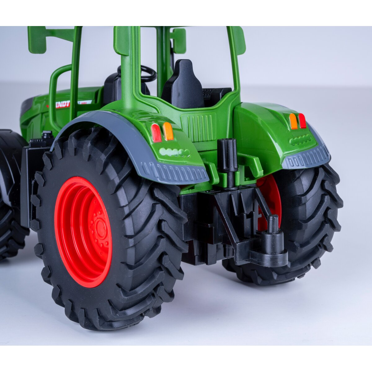 Zöld játék traktor piros felnikkel és nagy kerekekkel, hátulnézet.