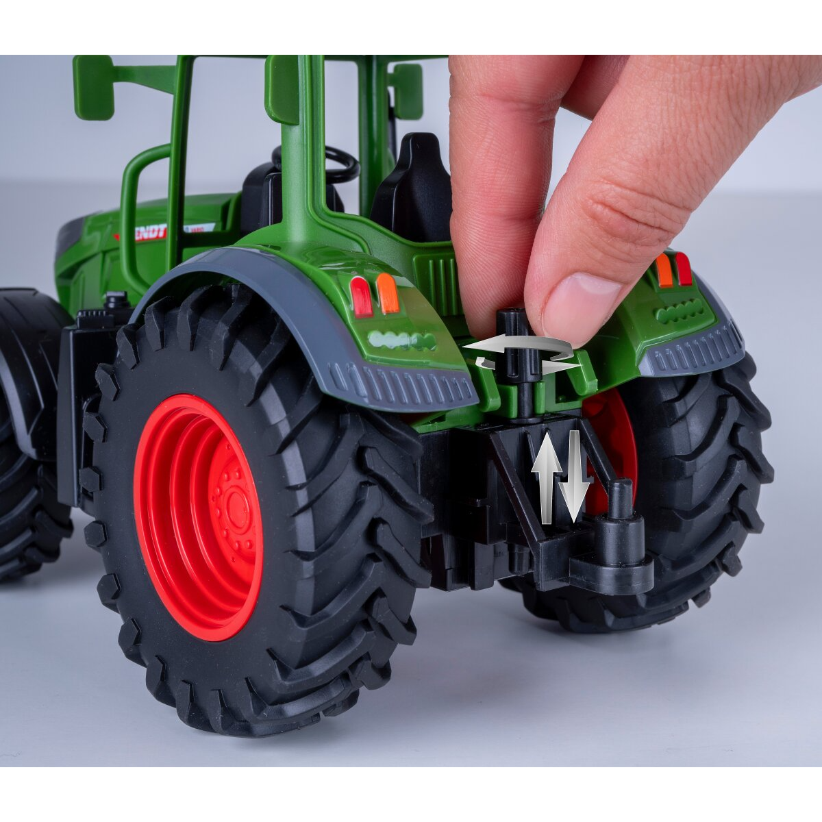 Egy kéz egy zöld játék traktor vonószerkezetének gombját tekeri.