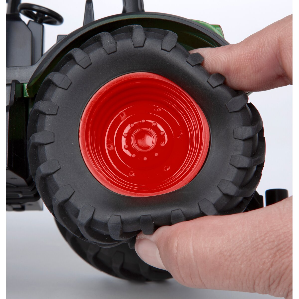 Játék-traktor kerék közelről, piros felni, fekete gumi, ujjak fogják.