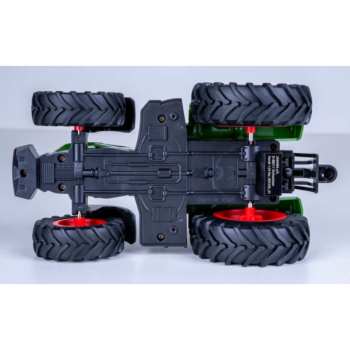 Zöld játék-traktor alsó része, fekete gumikerekekkel és piros felnikkel.