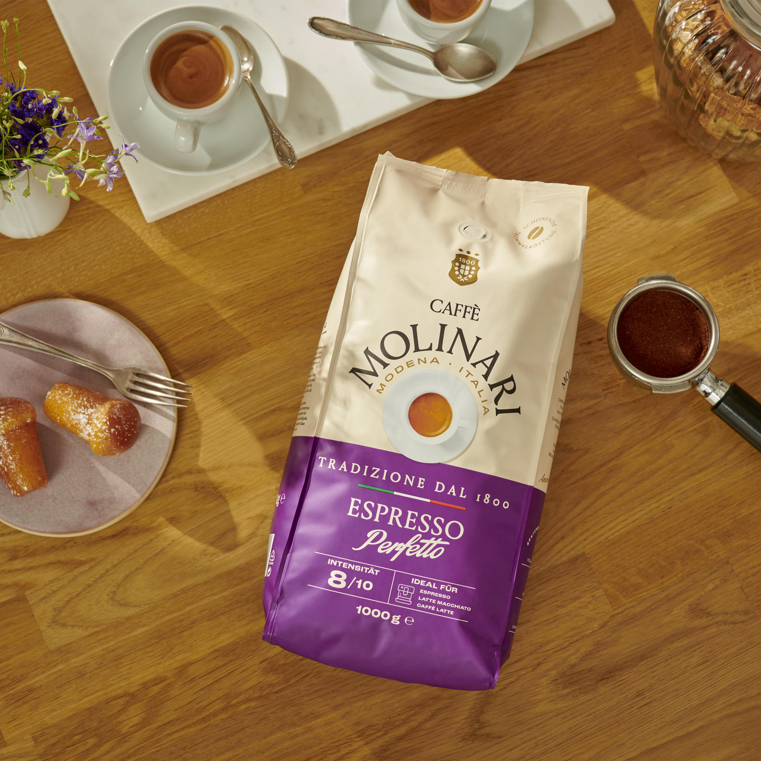 Kaffeepackung mit Espresso, Gebäck, Blumen und Kaffeemaschinenteil.