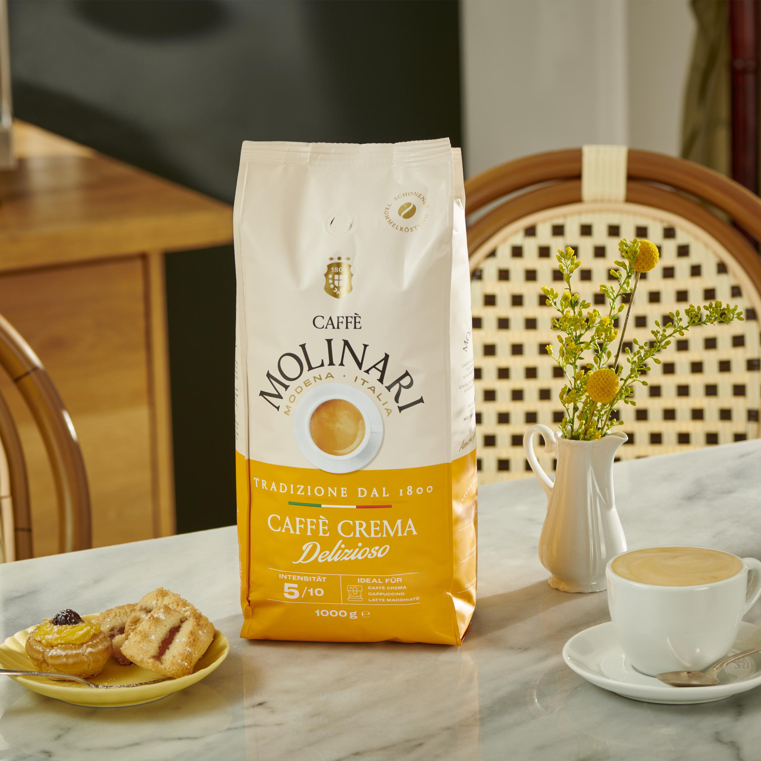 Eine Packung Molinari Kaffee steht auf einem Marmortisch mit Gebäck und einer Kaffeetasse.