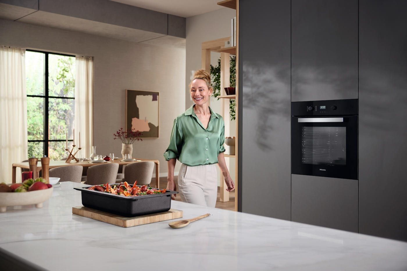 Eine Frau in einem grünen Hemd steht in einer modernen Küche neben einem Backofen.