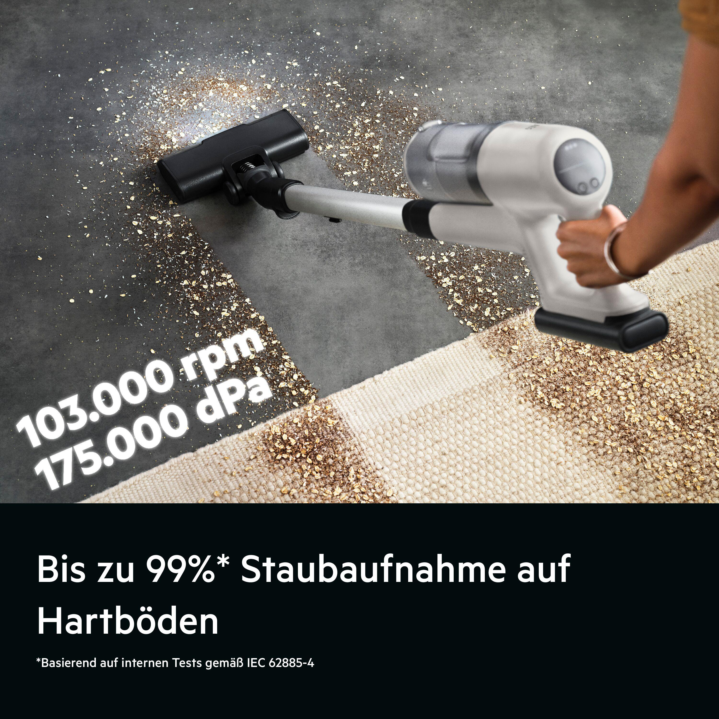 Ein weißer Handstaubsauger saugt Krümel von einem Teppich auf Hartboden.