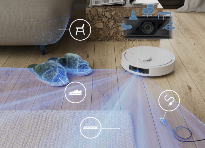 Egy fehér robotporszívó szkenneli a padlót. Papucs és egy cipő kiemelve.