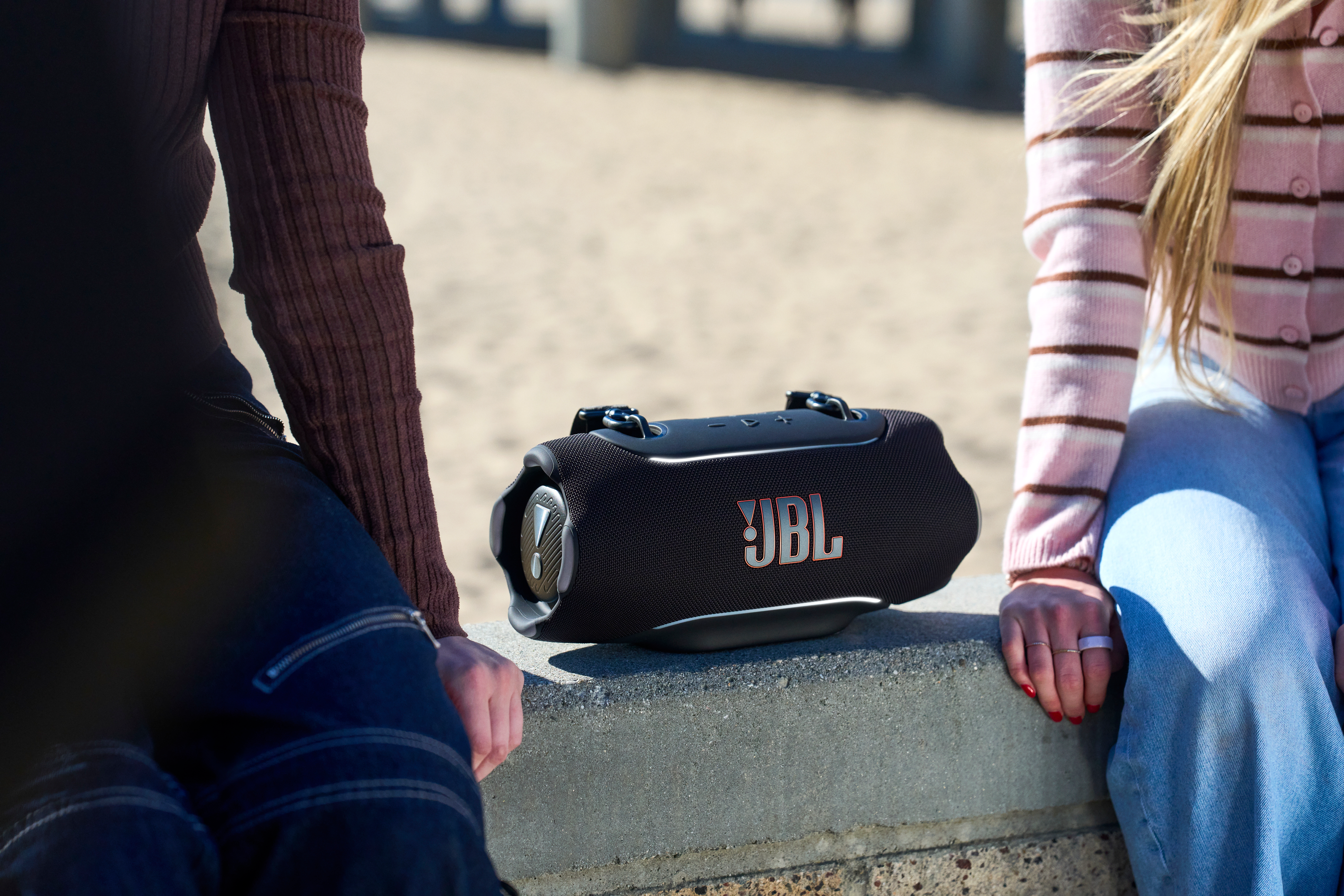 Une enceinte JBL noire posée sur un mur de béton, deux personnes assises à côté.