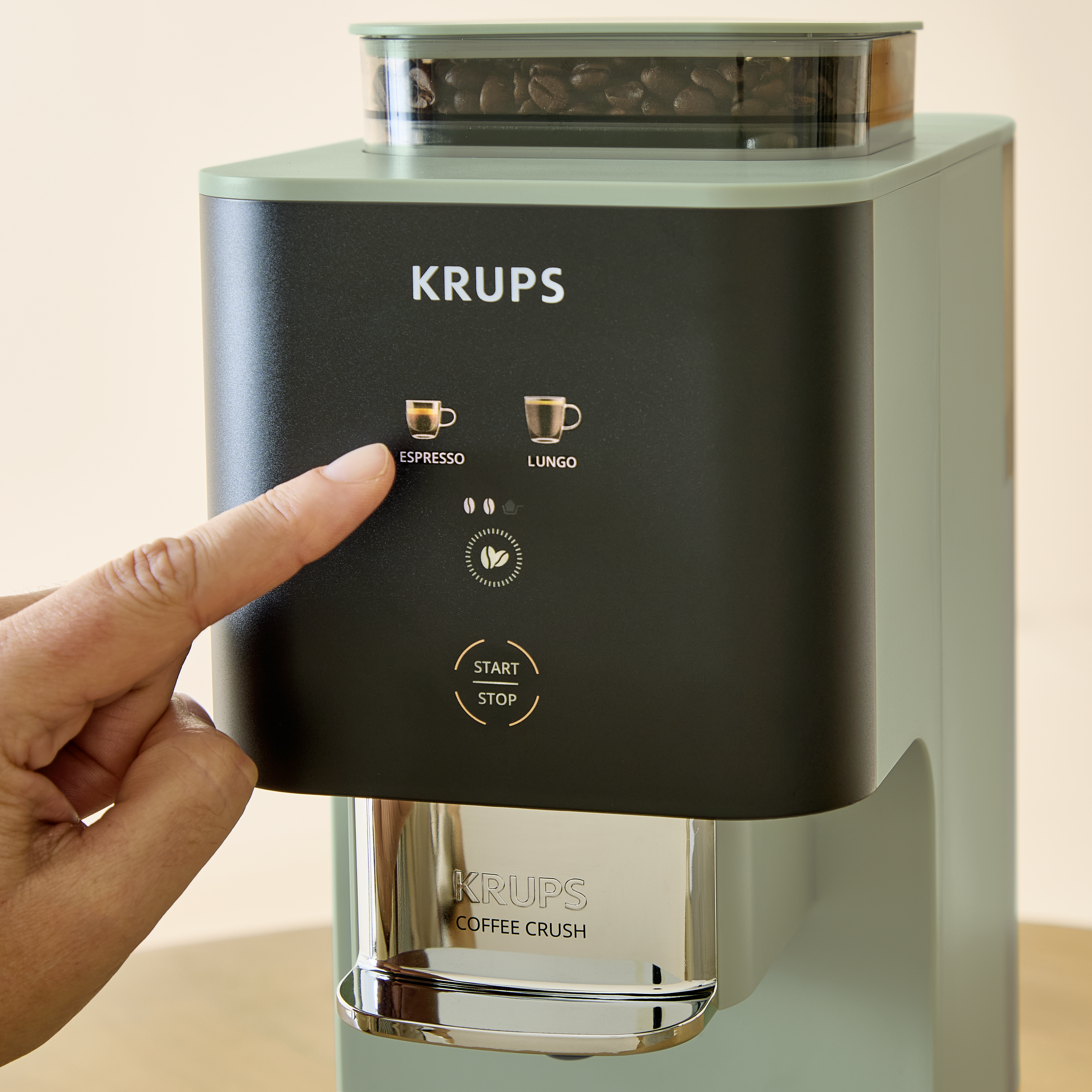 Una mano presiona una cafetera Krups verde que muestra opciones de espresso y lungo.