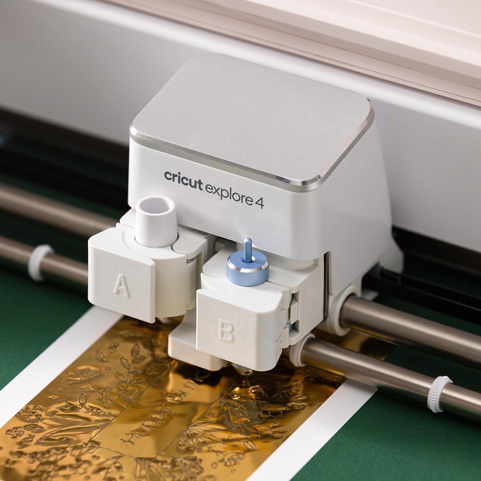 Una máquina de corte Cricut Explore 3 blanca procesa papel dorado de aluminio con diseño floral.