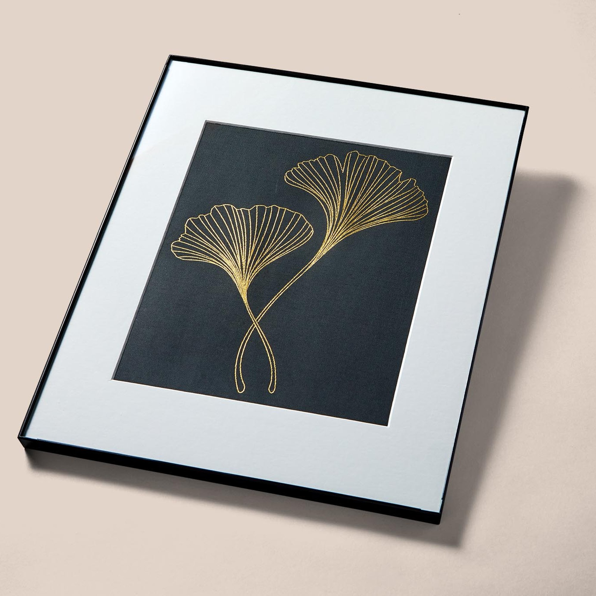 Obra de arte enmarcada con dos hojas de ginkgo doradas sobre fondo negro.