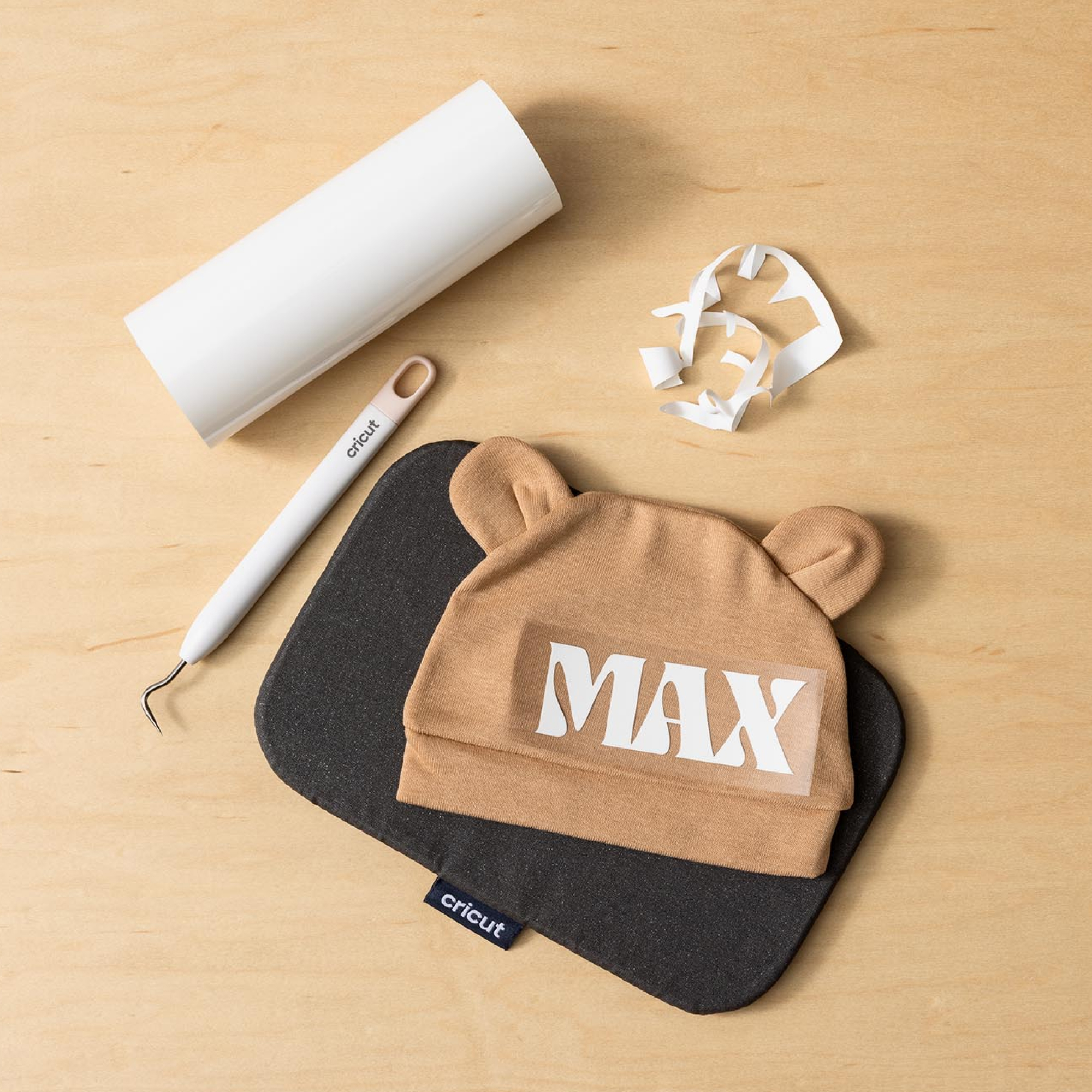 Gorro de bebé marrón con orejas, calcomanía 'MAX', herramienta, rollo y recortes.