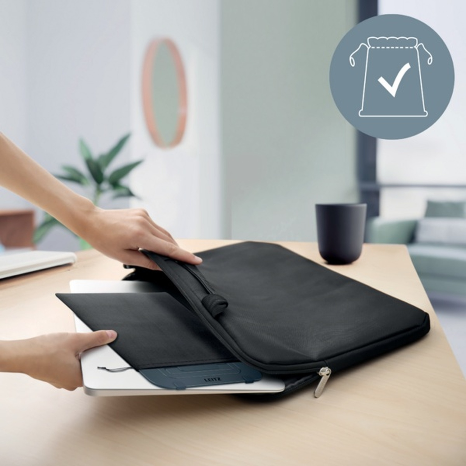 Una persona mette un laptop in una custodia nera su un tavolo di legno.