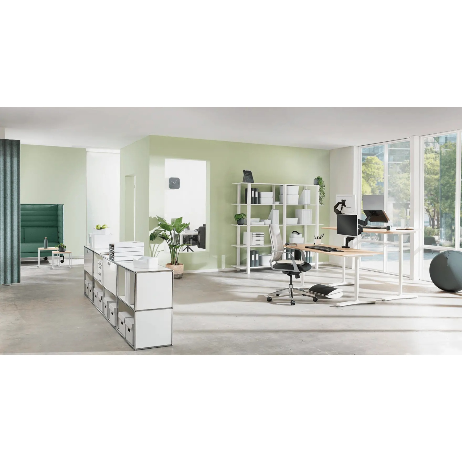 Ufficio moderno con scrivanie regolabili, area salotto verde e scaffale bianco.