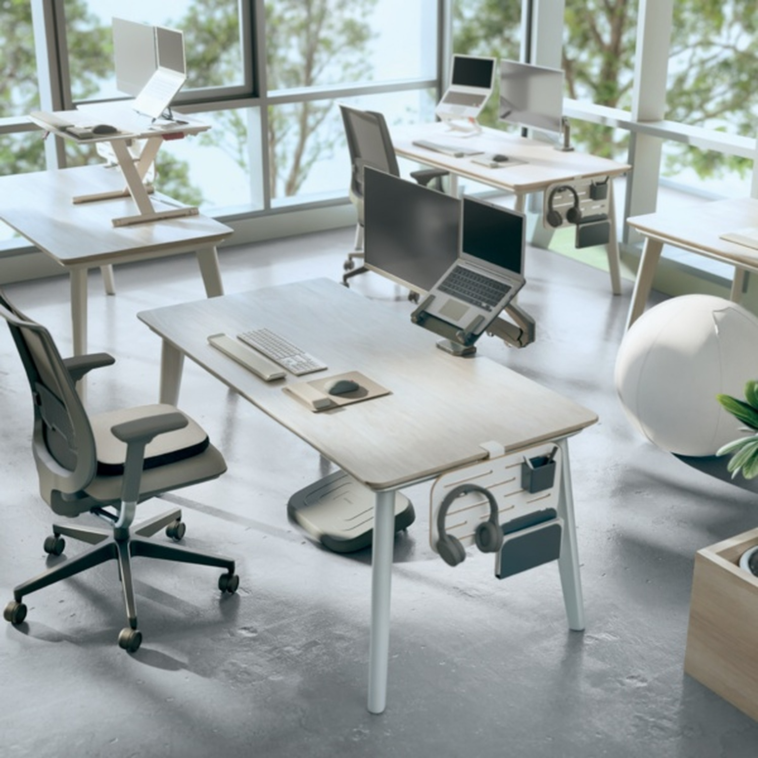 Ufficio moderno con scrivanie, laptop, monitor e sedie. Grandi finestre si affacciano sul verde.