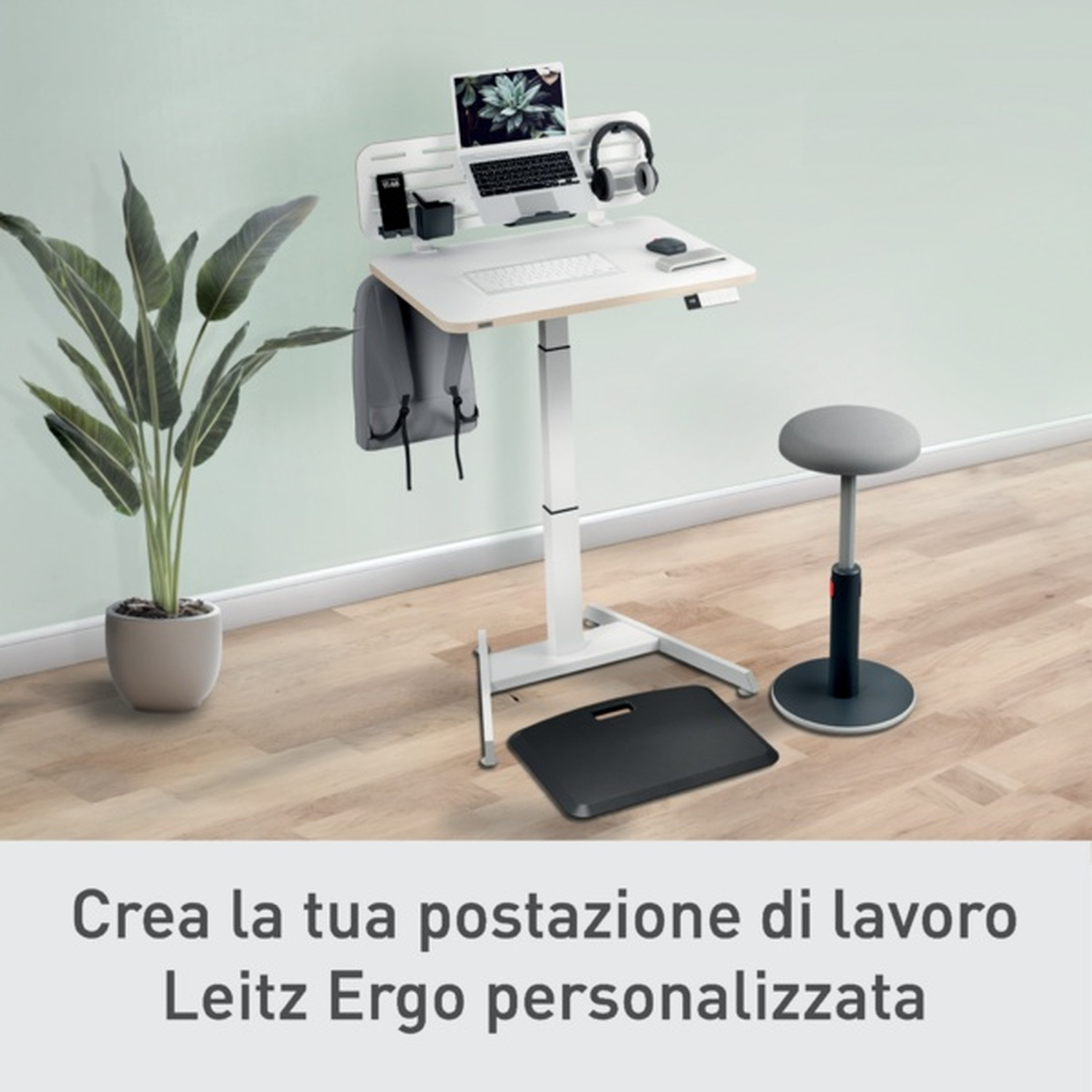 Una scrivania regolabile in altezza con laptop, cuffie e pianta.