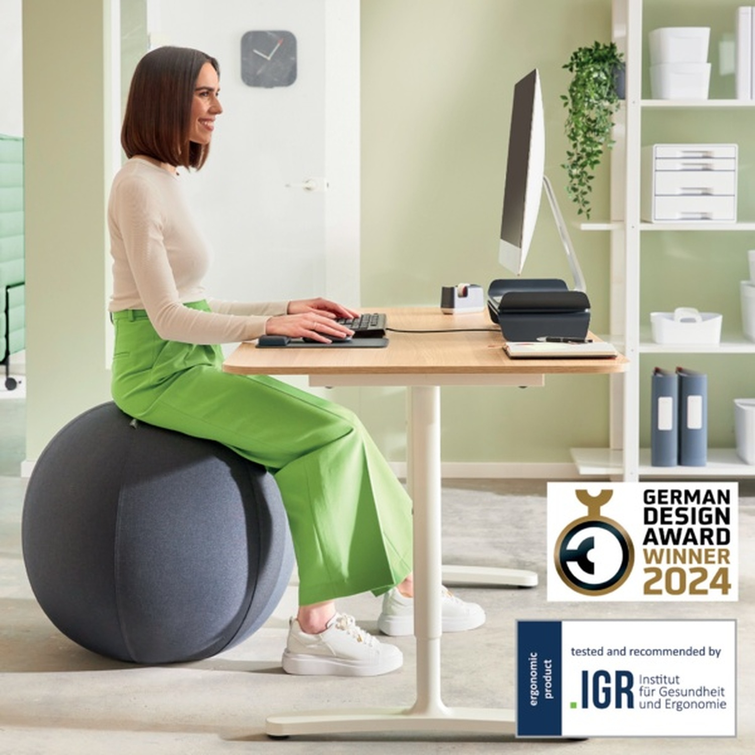 Donna seduta su palla da ginnastica alla scrivania, digita. Vincitore German Design Award 2024.