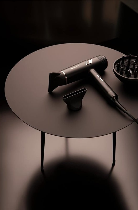 Czarna suszarka do włosów z nasadkami i dyfuzorem stoi na ciemnym, okrągłym stole.