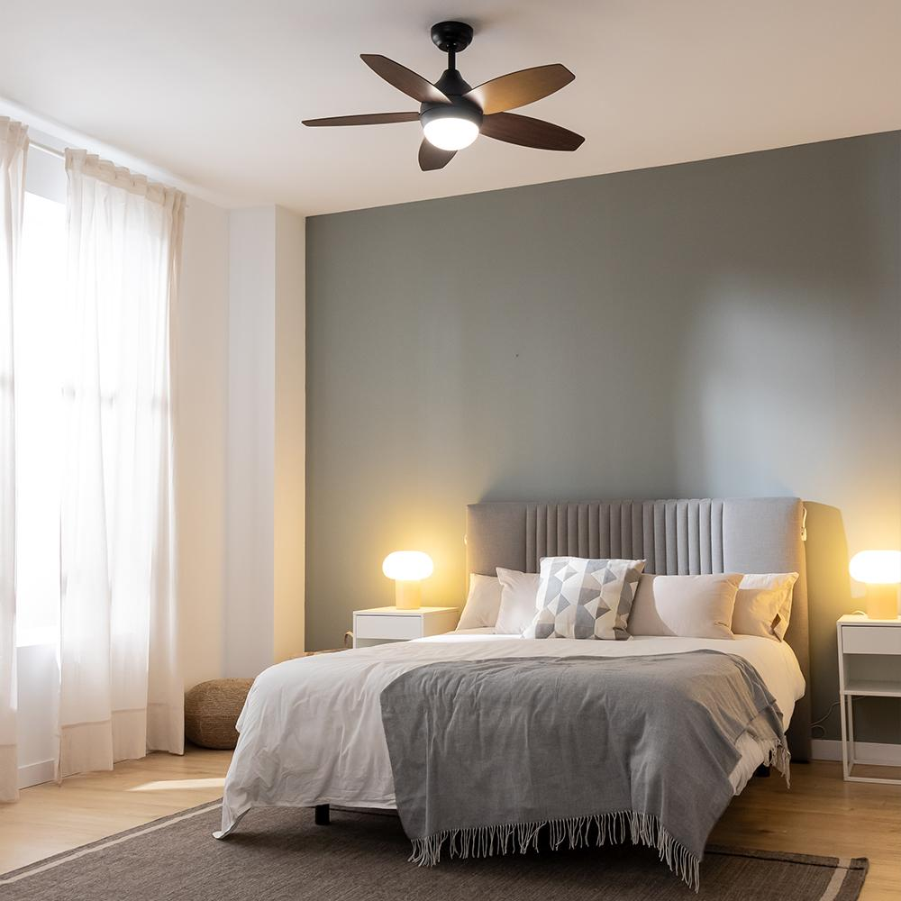 Un dormitorio moderno con cama, mesitas, lámparas y ventilador de techo.