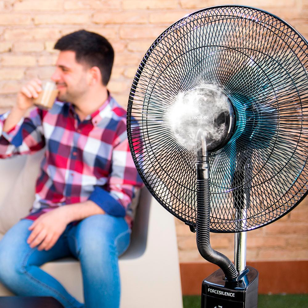 Un hombre se sienta en una silla bebiendo. Un ventilador rocía agua.