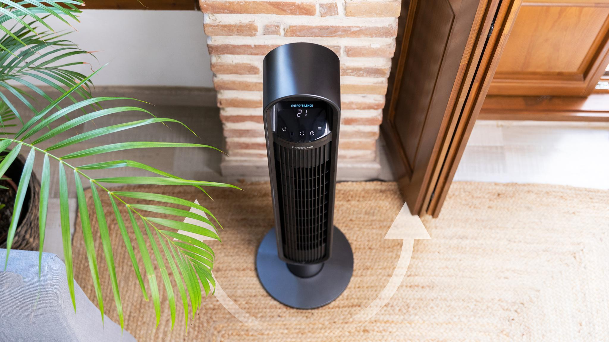 Ventilador de torre negro con pantalla digital sobre alfombra de yute junto a planta.
