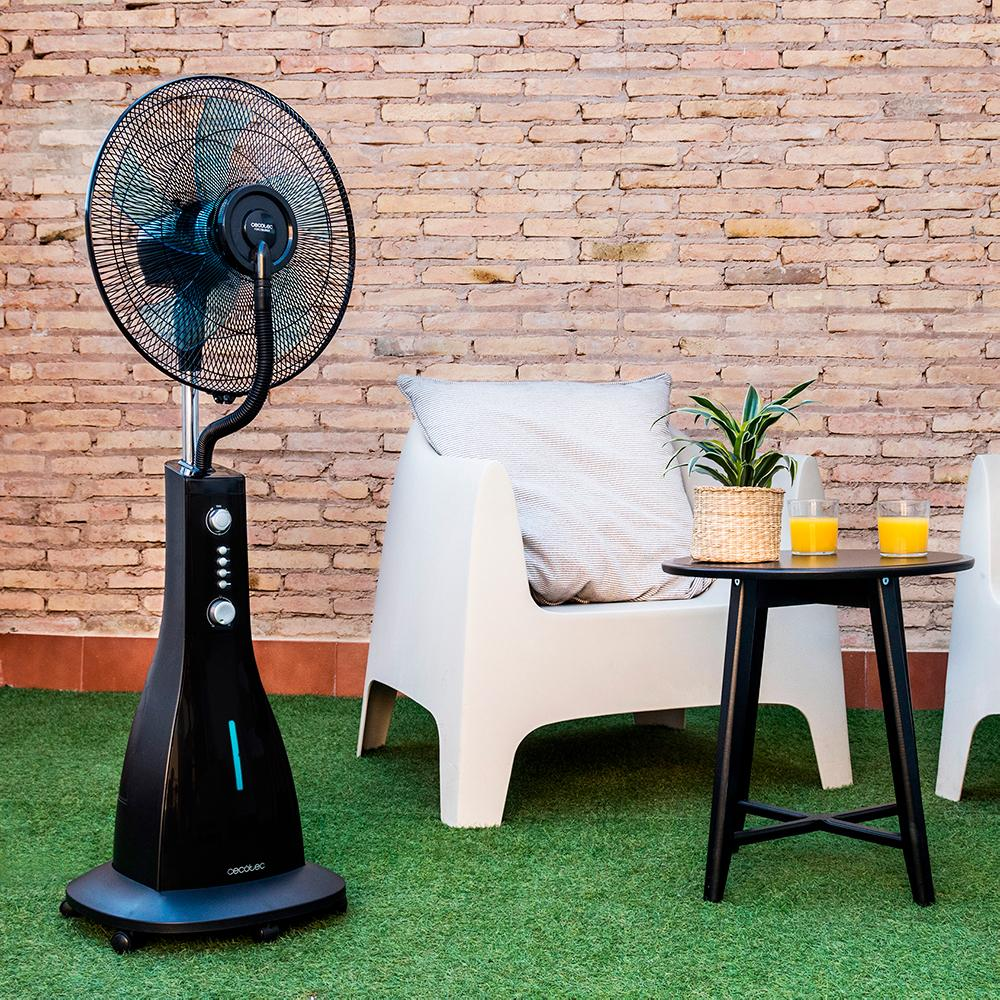 Ventilador nebulizador negro sobre césped artificial junto a sillas blancas y mesa con bebidas.