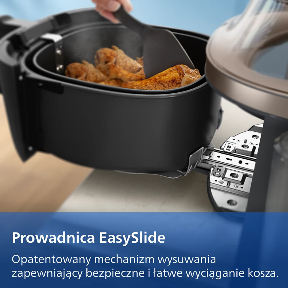 Kosz frytkownicy powietrznej z kawałkami kurczaka jest wyjmowany. Para unosi się.