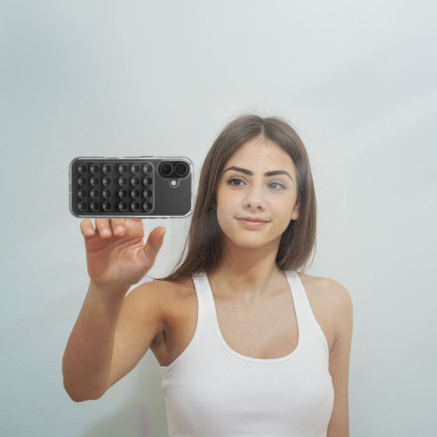 Una joven con camiseta blanca sostiene una funda de teléfono con relieves sobre fondo claro.