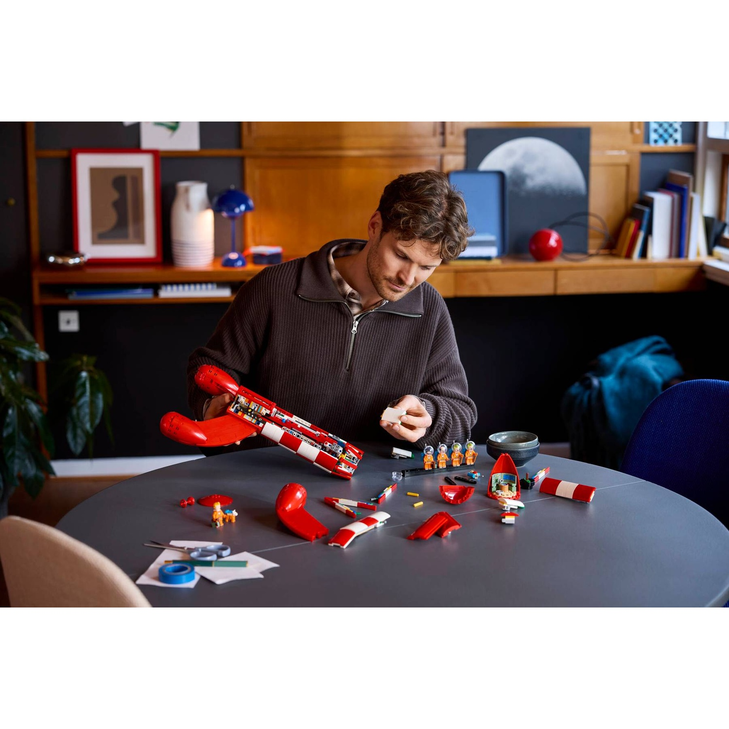 Man builds a red and white spaceship model from Lego bricks.