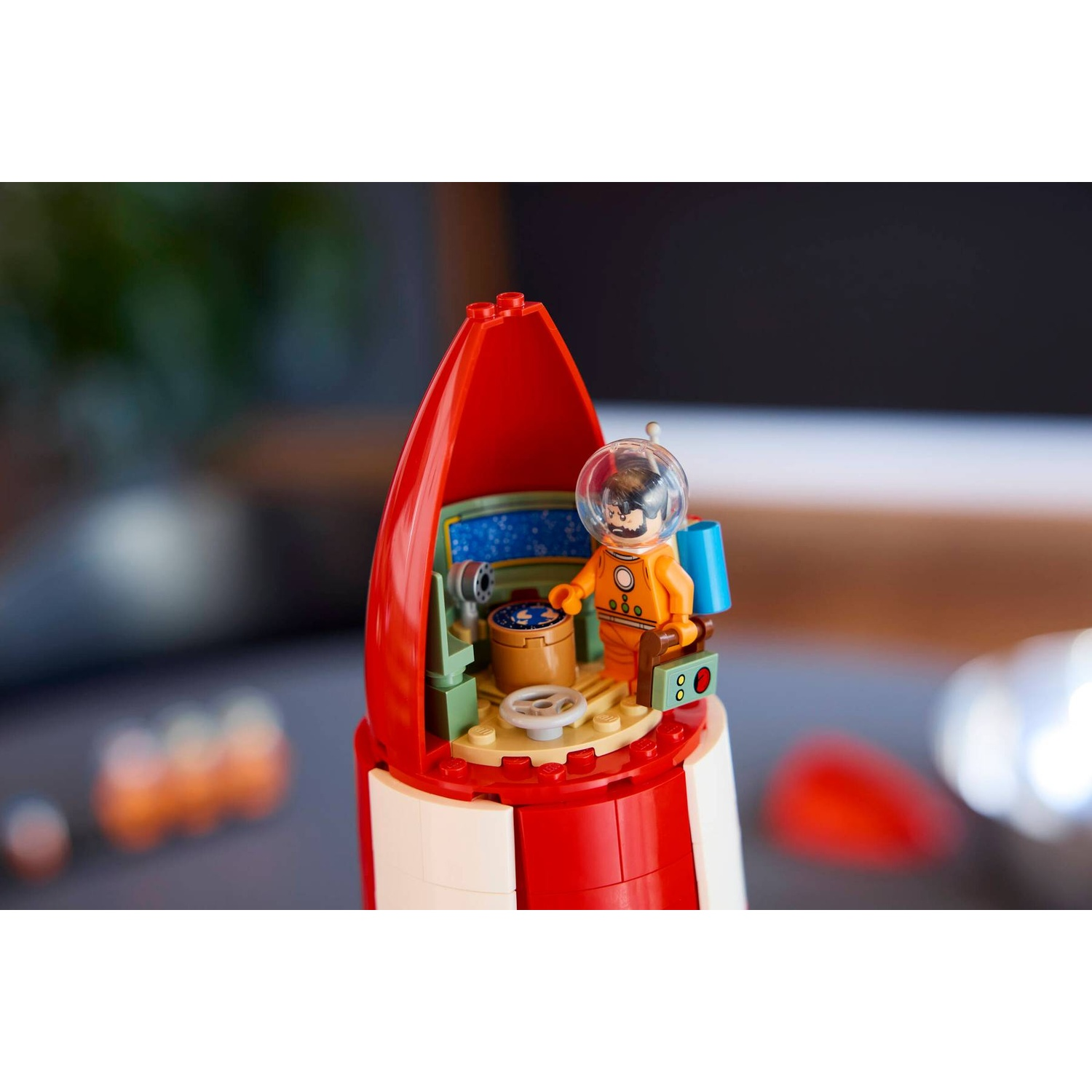A Lego astronaut inside a red and white rocket ship cockpit.